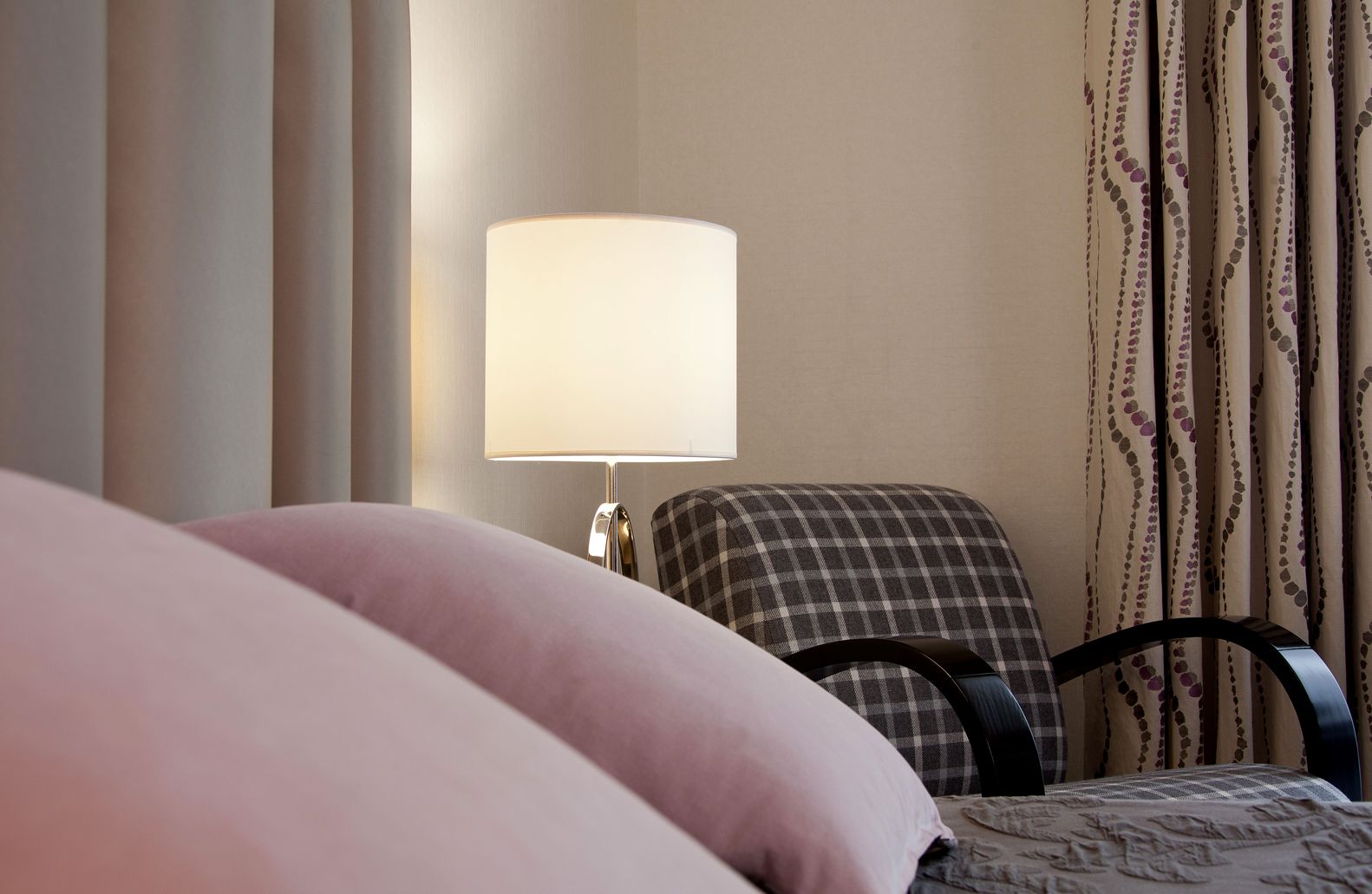 A hotel room with a bed, a chair, a lamp, and curtains.