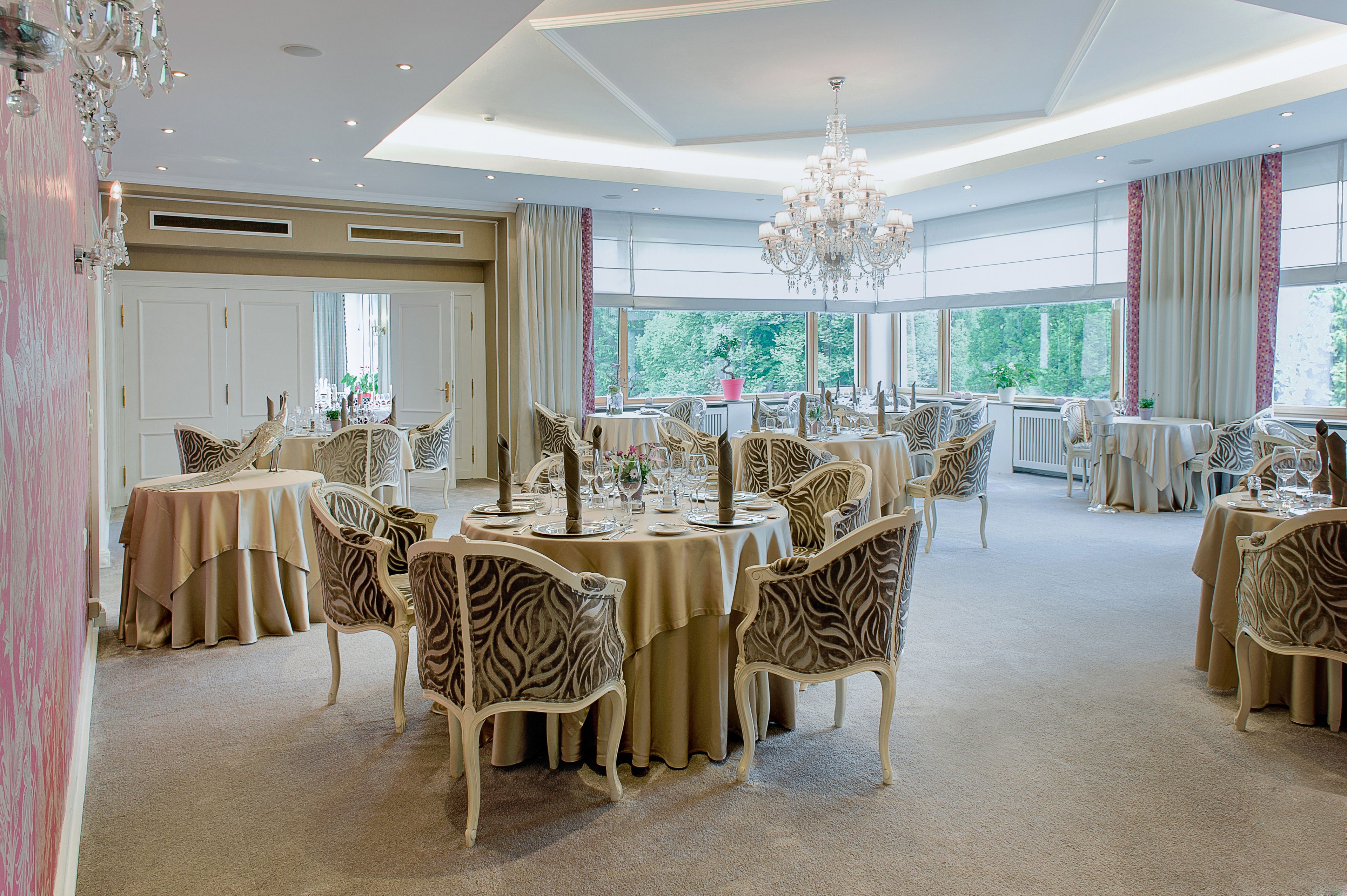 A spacious dining area with round tables, zebra-patterned chairs, and a chandelier.