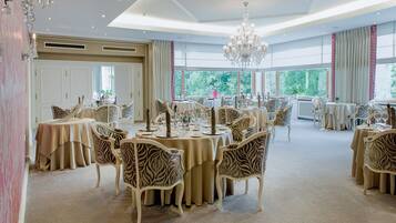 A spacious dining area with round tables, zebra-patterned chairs, and a chandelier.