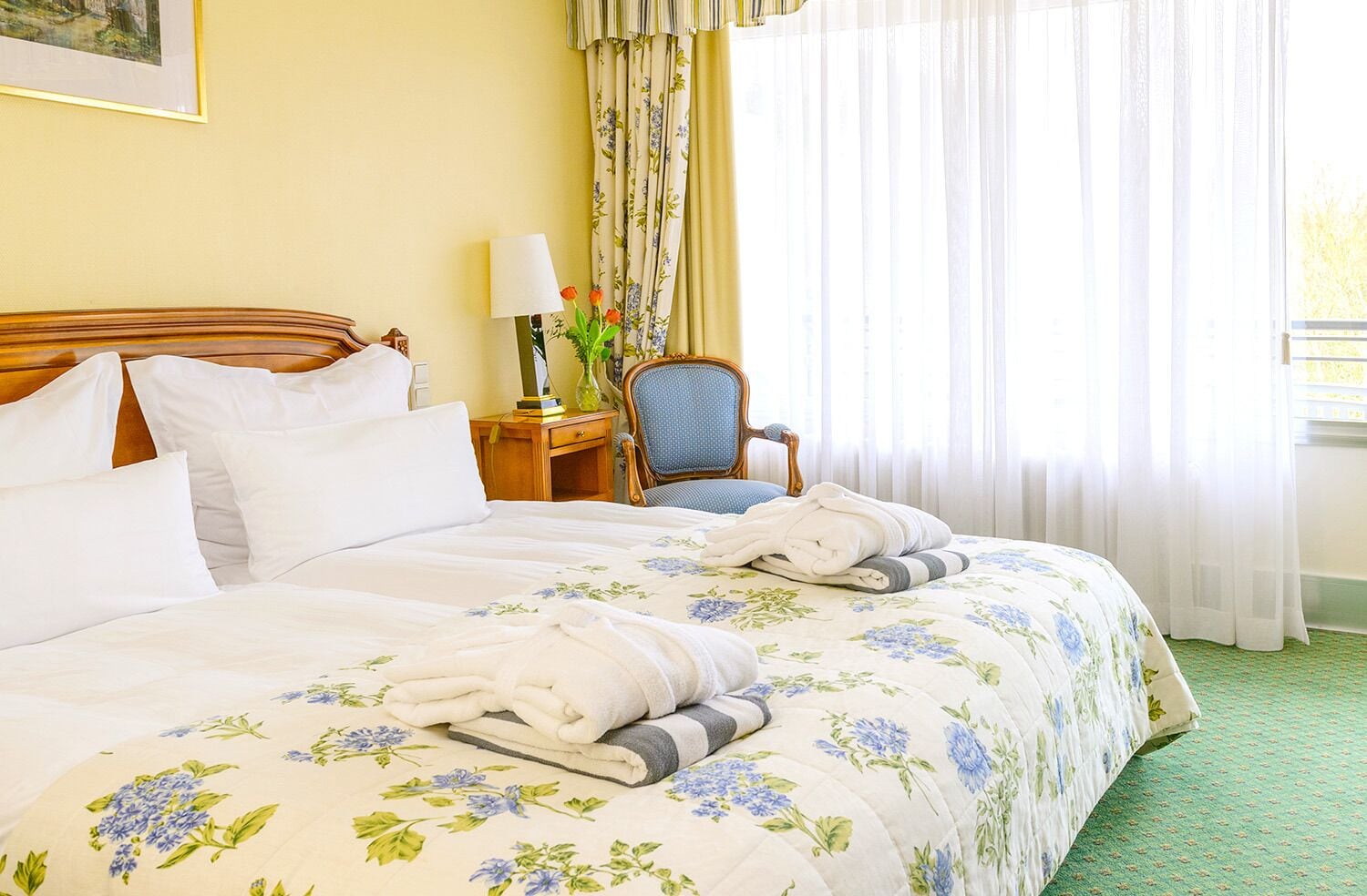 Habitación de hotel con una cama grande, una silla, una mesita de noche y una ventana con cortinas.