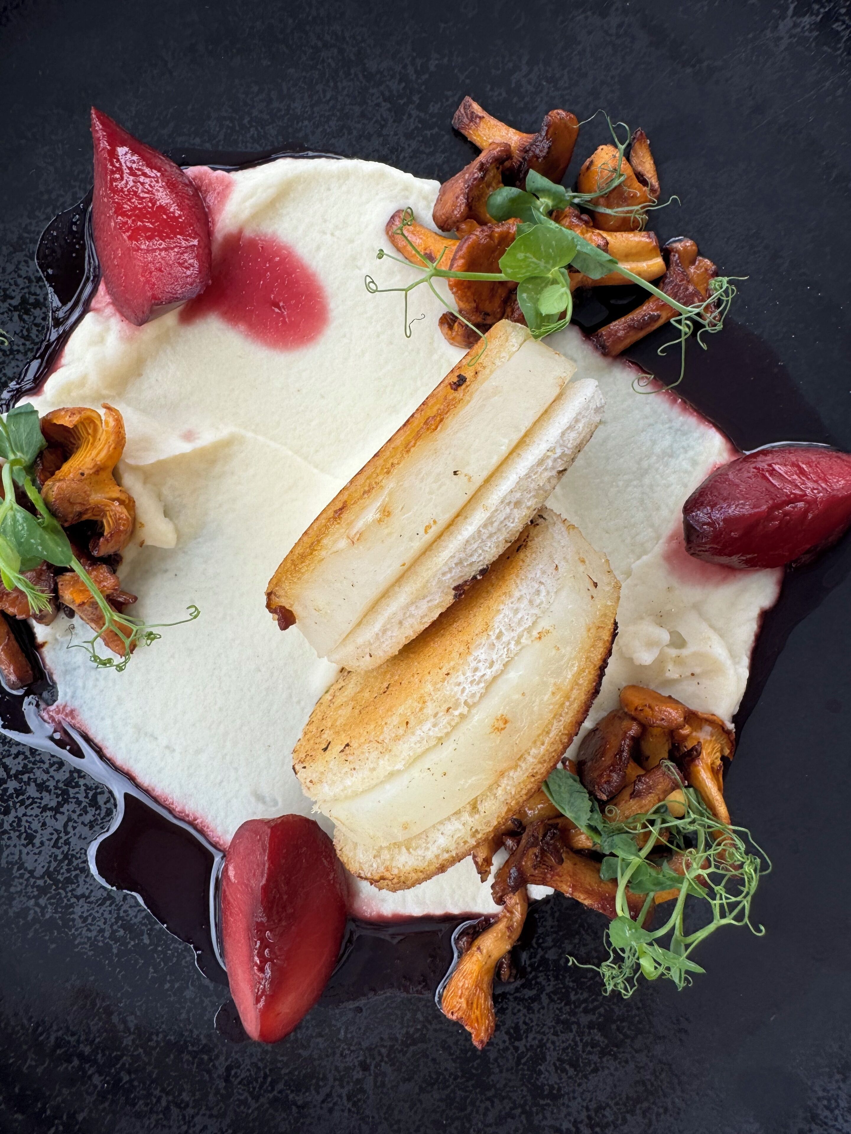 A dessert plate with a creamy white base, topped with slices of bread, and surrounded by various mushrooms and greens.