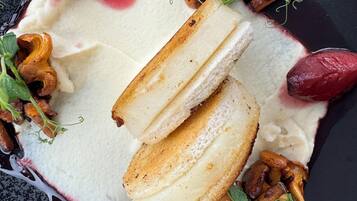 A dessert plate with a creamy white base, topped with slices of bread, and surrounded by various mushrooms and greens.
