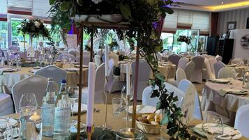 A banquet hall with round tables set for dining, each with a candle centerpiece and glassware.