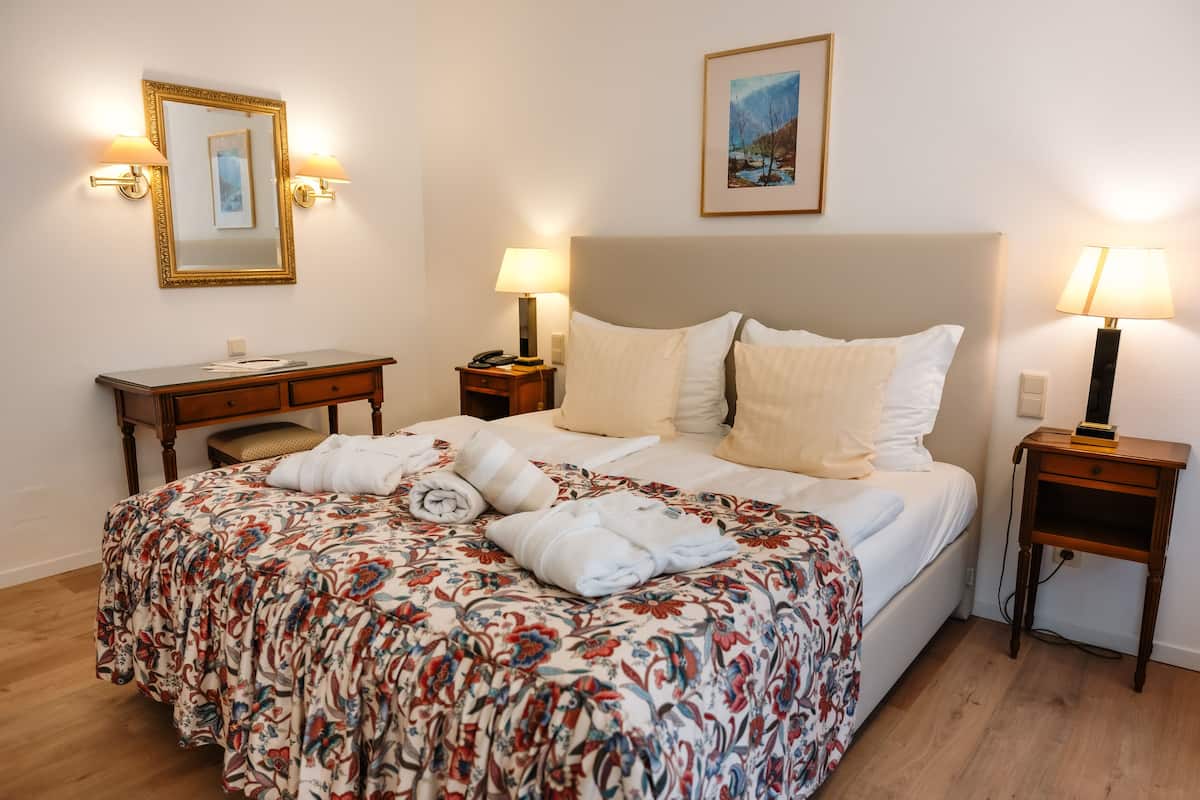 Una habitación de hotel con una cama, dos mesitas de noche, un escritorio y una silla.