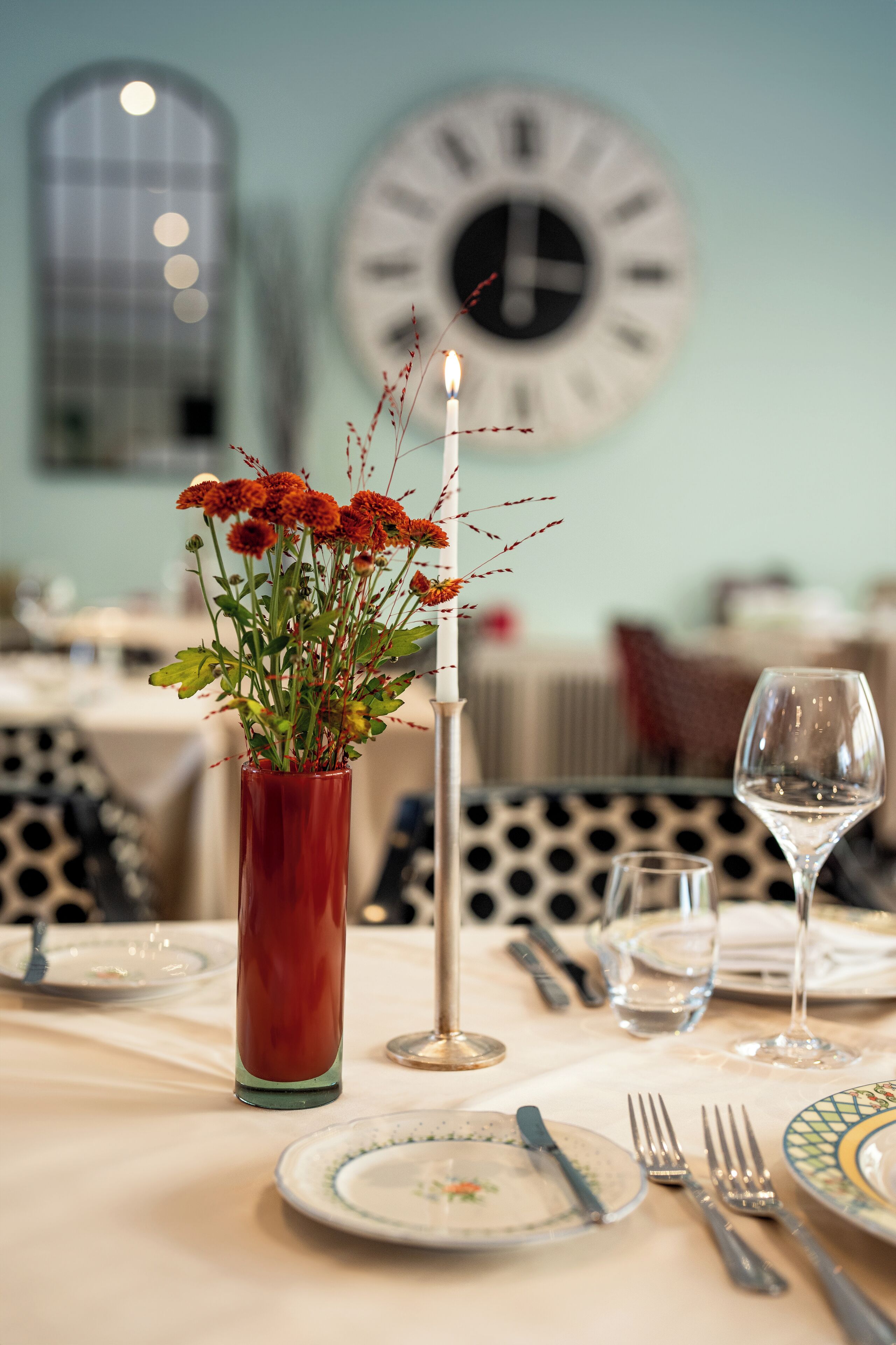 Una mesa de comedor dispuesta con platos, cubiertos, un florero con flores y una vela.