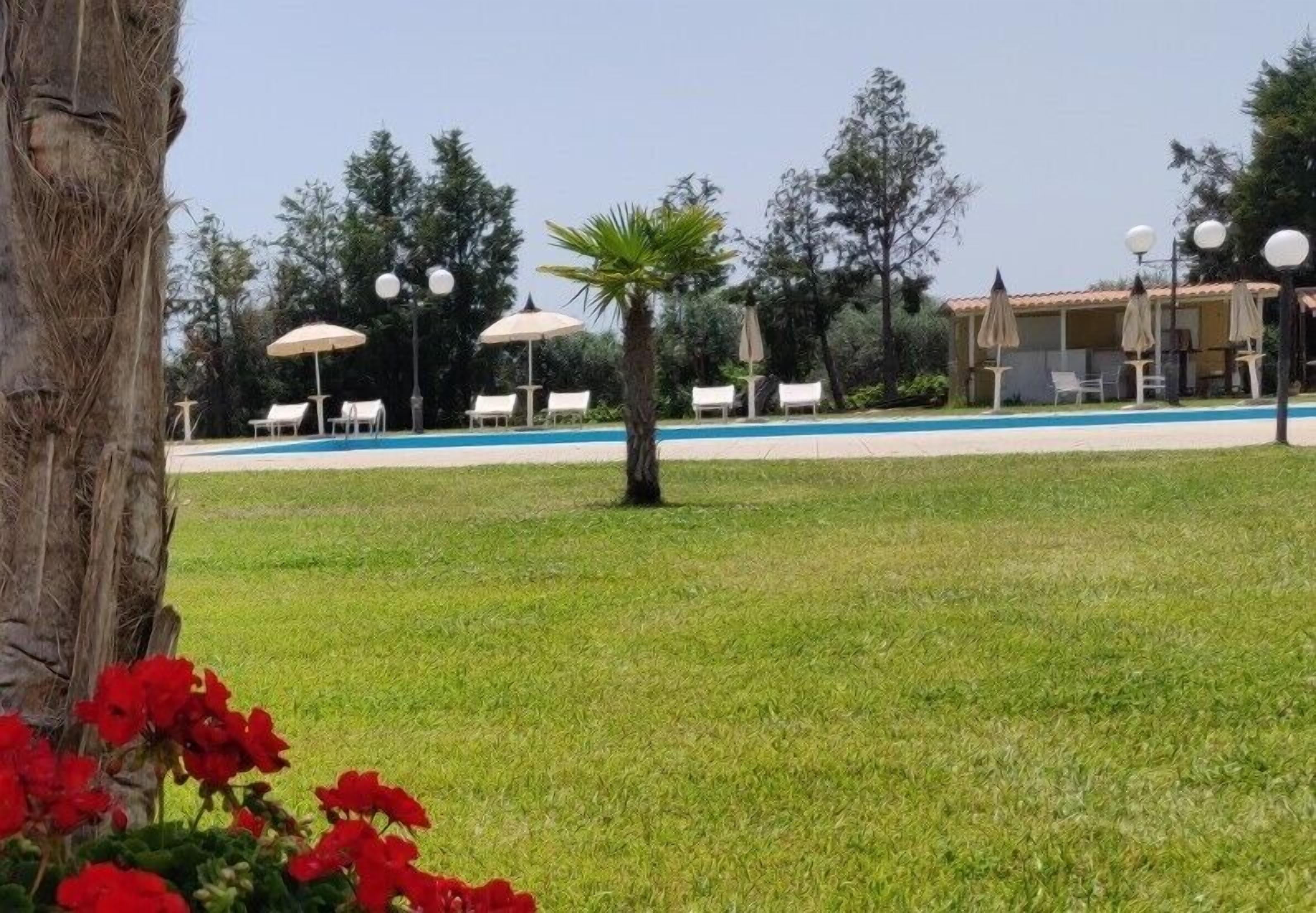 A pool area with lounge chairs and umbrellas, surrounded by trees and a building with a tiled roof.