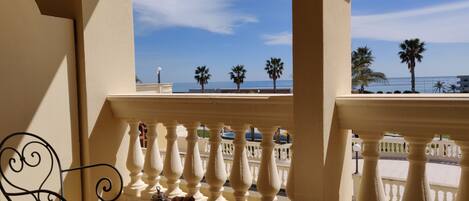A balcony with a table set for breakfast, overlooking a beach with palm trees and the sea.