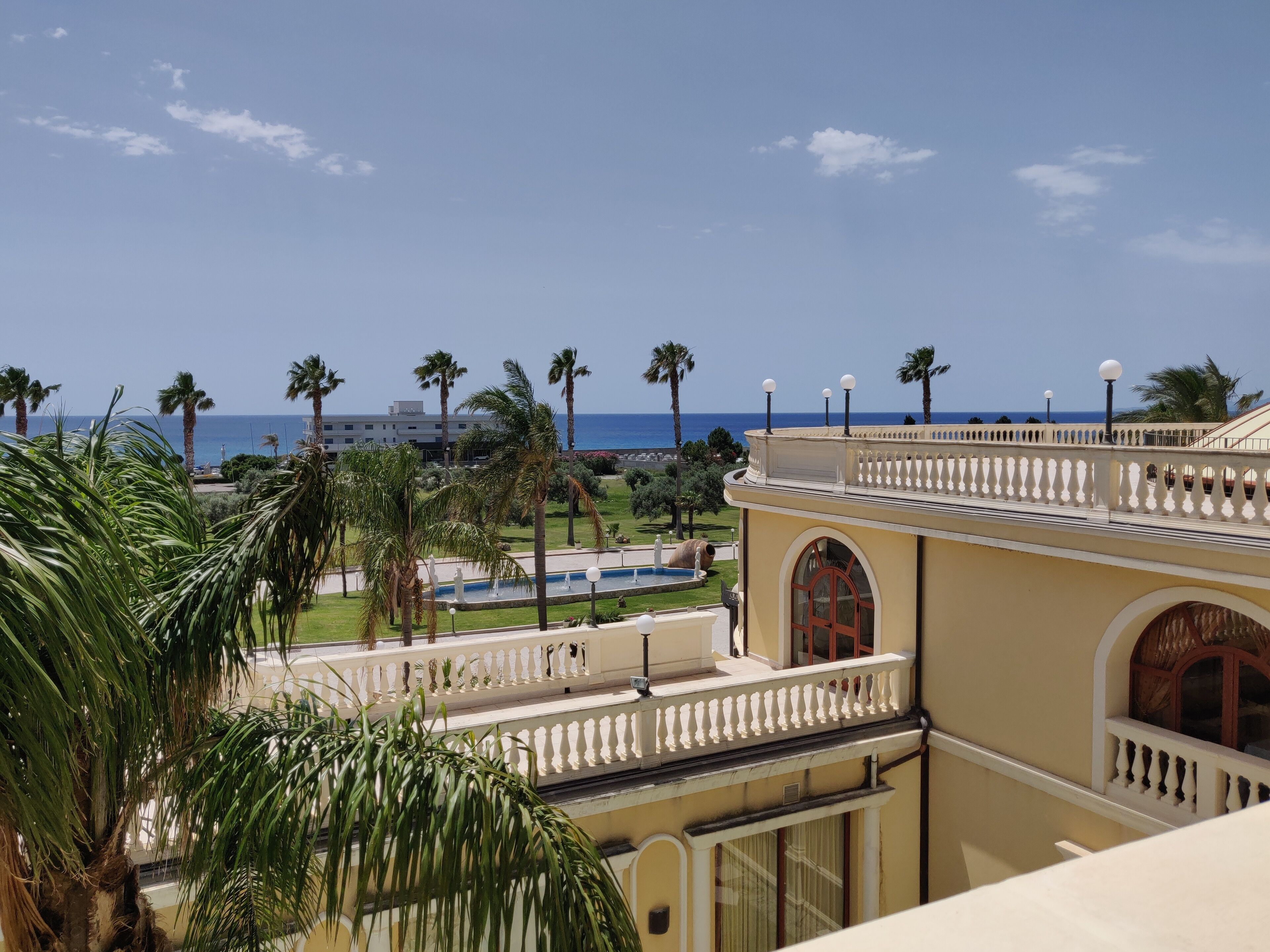 A hotel with a view of the sea, palm trees, and a pool.