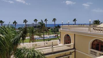 A hotel with a view of the sea, palm trees, and a pool.