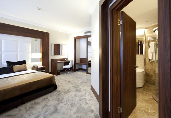 A hotel room with a large bed, a desk, a chair, a mirror, and a bathroom with a shower and sink. - Ikbal Thermal Hotel & Spa (Afyonkarahisar)