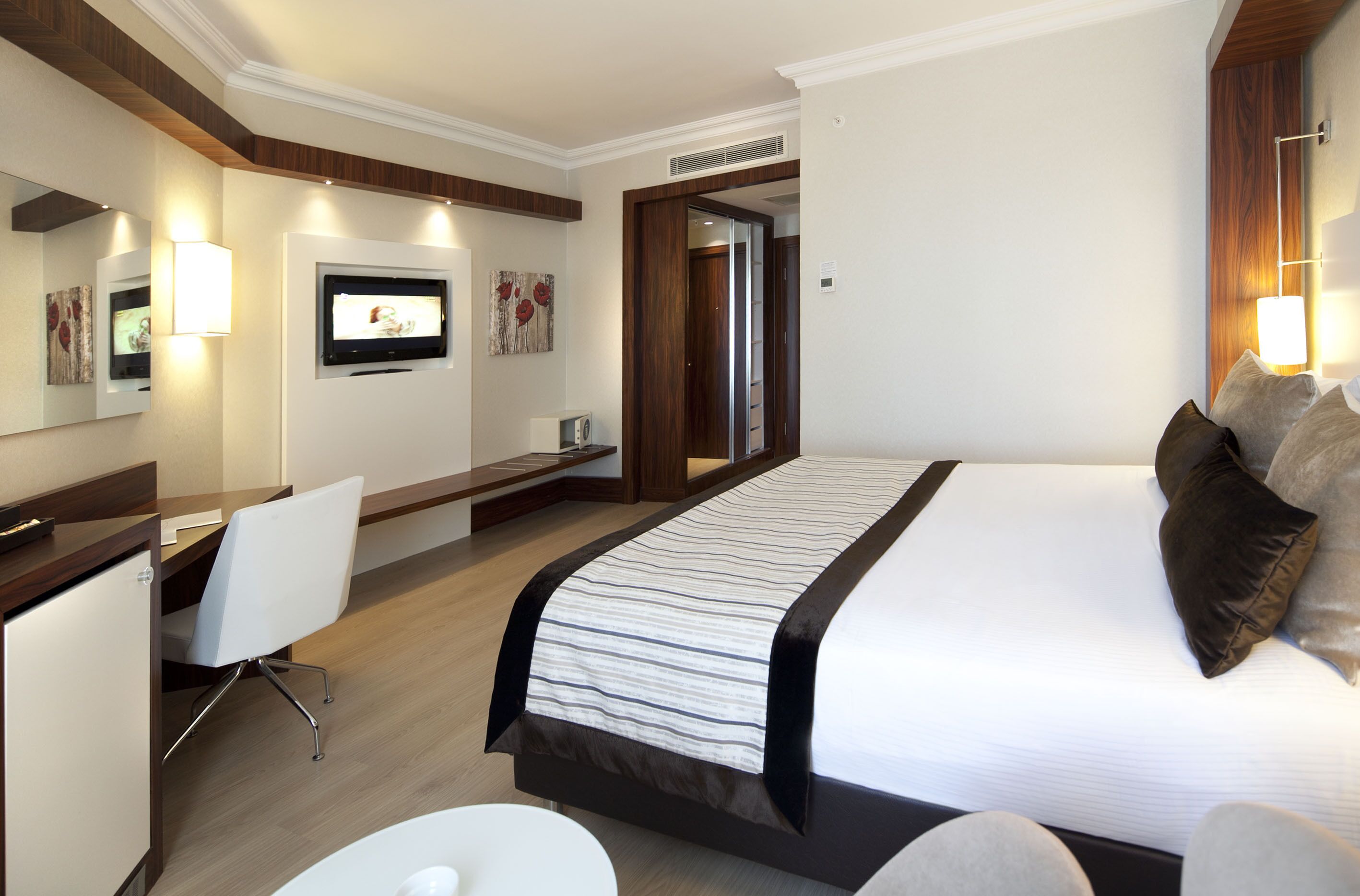 A hotel room with a large bed, a desk with a chair, a television, and a mirror.