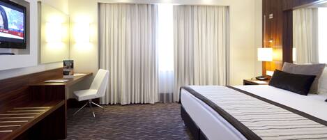 A hotel room with a bed, a desk, a chair, a TV, and a large window with curtains.