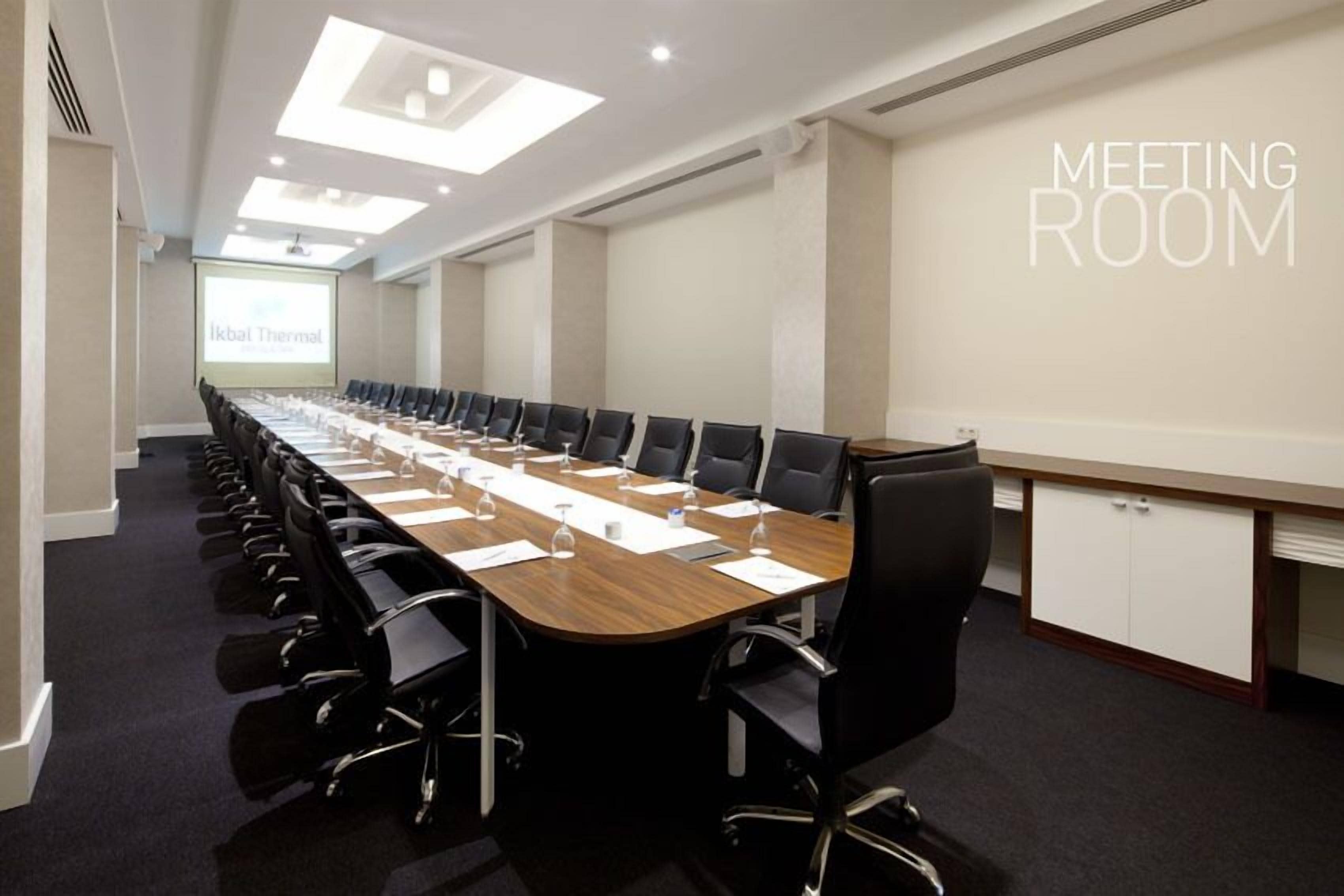 A meeting room with a long table, black chairs, and a projector screen.