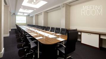 A meeting room with a long table, black chairs, and a projector screen.