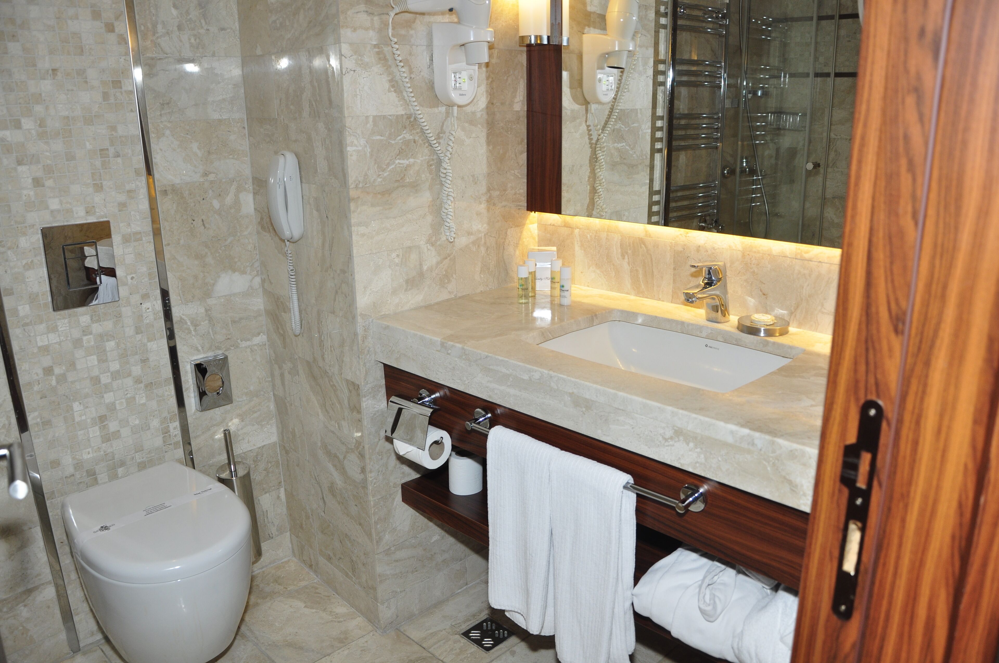 A modern bathroom with a marble sink, a mirror, a toilet, and a shower.