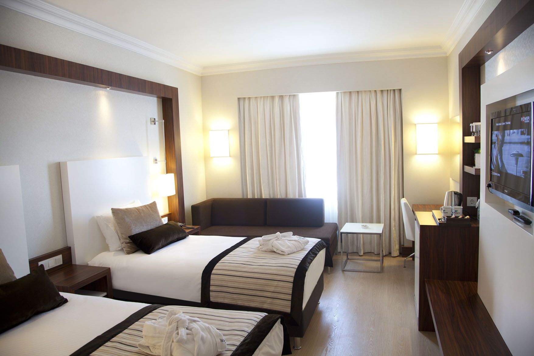 A hotel room with two beds, a sofa, a desk, a TV, and curtains.