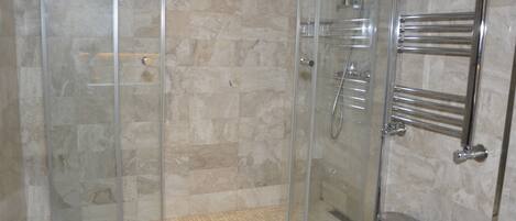 A glass-enclosed shower with a tiled floor, a chrome towel rack, and a small trash bin.