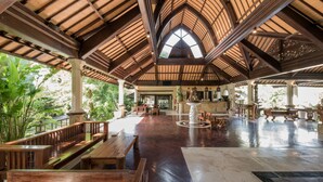 Espacio abierto con bancos y mesas de madera, una fuente central y un techo alto abovedado con luz natural.