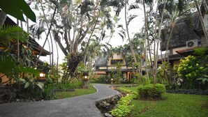 Un sendero conduce a un edificio de estilo tradicional rodeado de exuberante vegetación tropical.