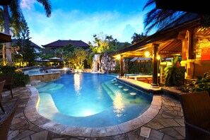 A swimming pool with a stone border, surrounded by lounge chairs and a covered seating area with a view of the pool. - Hotel Villa Lumbung Bali Seminyak (Keroboken Kelod)