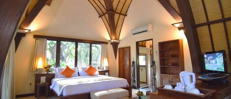A spacious bedroom with a large bed, a desk with a coffee maker, and a television.