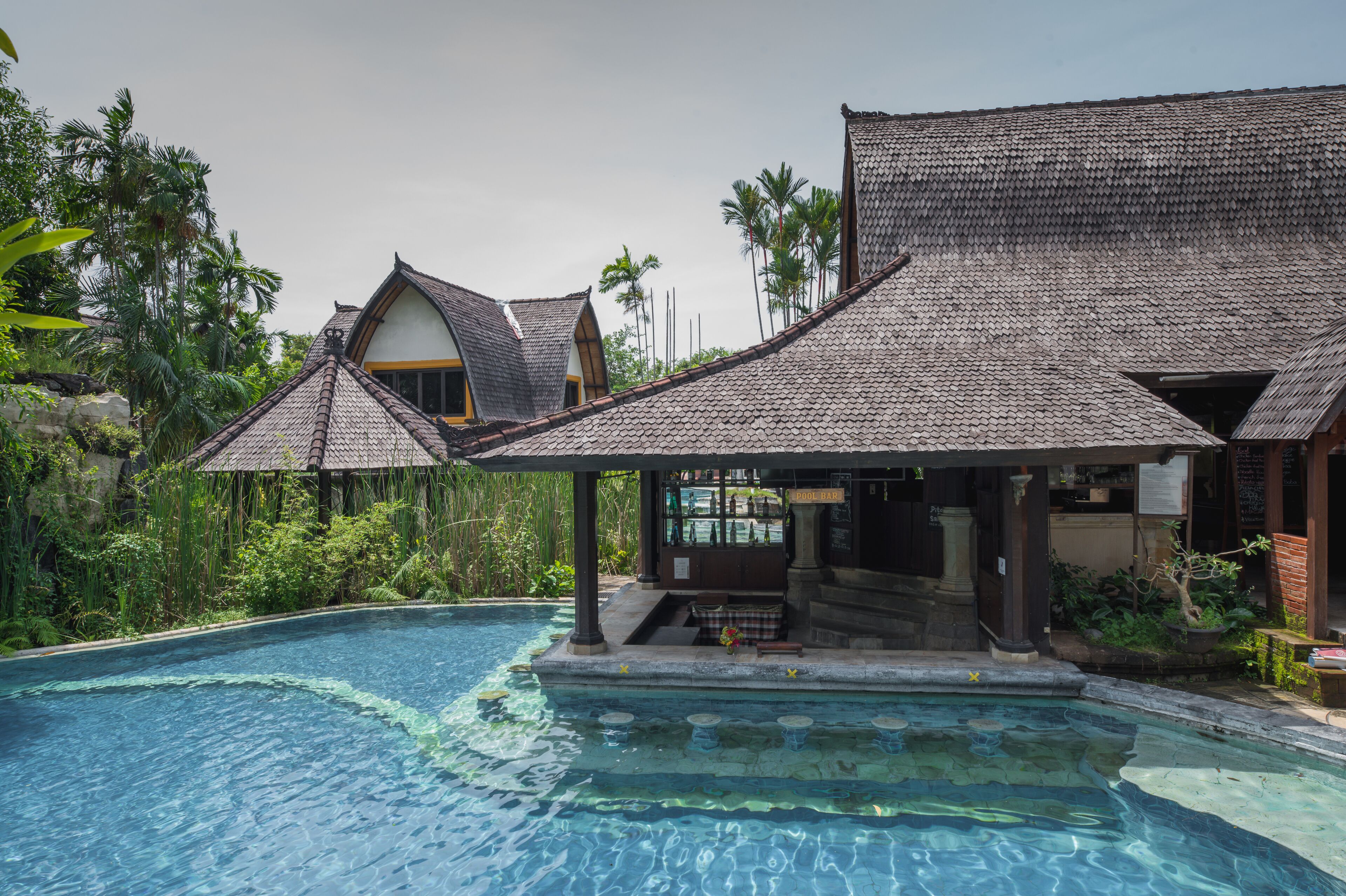 A poolside area with a covered seating area and a building with a tiled roof.