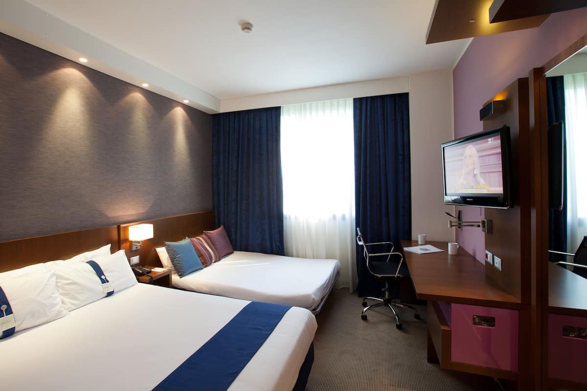 Une chambre d’hôtel avec deux lits, un bureau, une télévision et une fenêtre avec des rideaux.