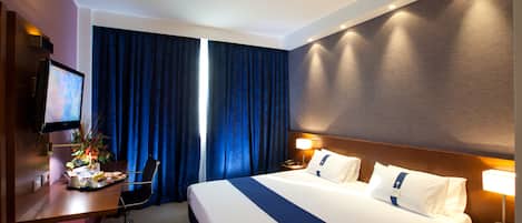 Habitación de hotel con una cama grande, un escritorio con computadora, una silla y un televisor.