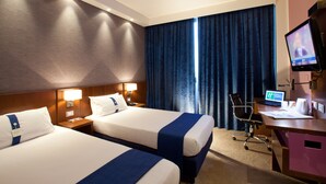 Habitación de hotel con dos camas, un escritorio con ordenador, una silla y un televisor.