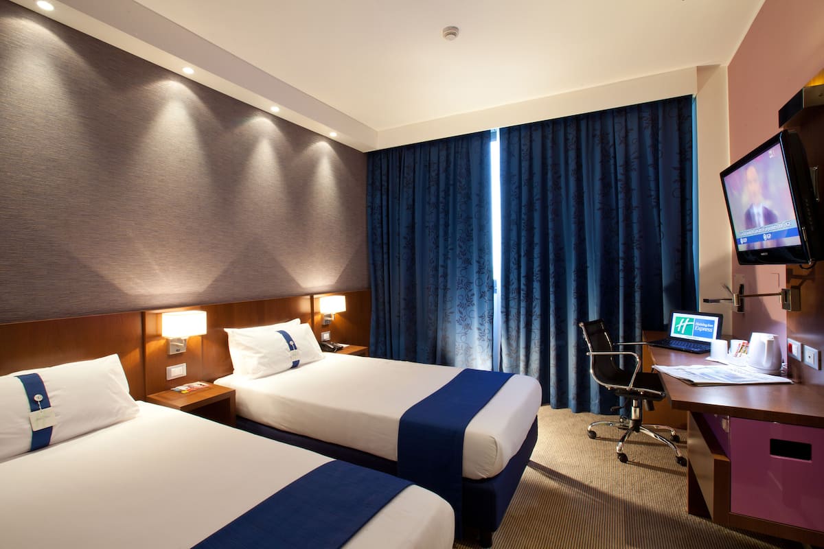 Une chambre d’hôtel avec deux lits, un bureau avec un ordinateur, une chaise et un téléviseur.