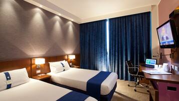 A hotel room with two beds, a desk with a computer, a chair, and a television.