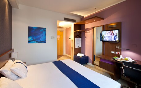A hotel room with a bed, a TV, a desk, and a bathroom.
