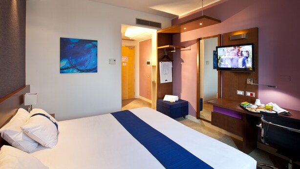 Habitación de hotel con cama, televisor, escritorio y baño.