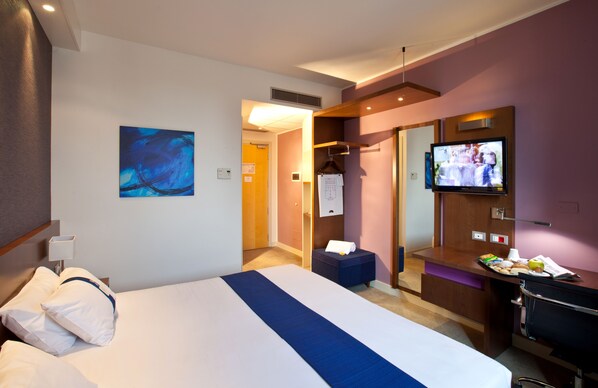 Habitación de hotel con cama, televisor, escritorio y baño.