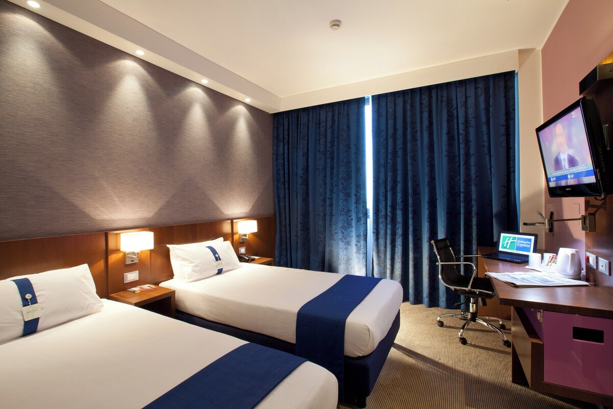 Habitación de hotel con dos camas, un escritorio con computadora, una silla y un televisor.