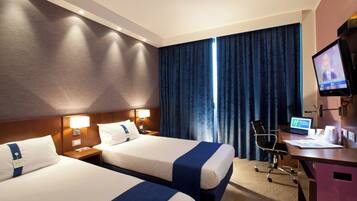 Habitación de hotel con dos camas, un escritorio con computadora, una silla y un televisor.