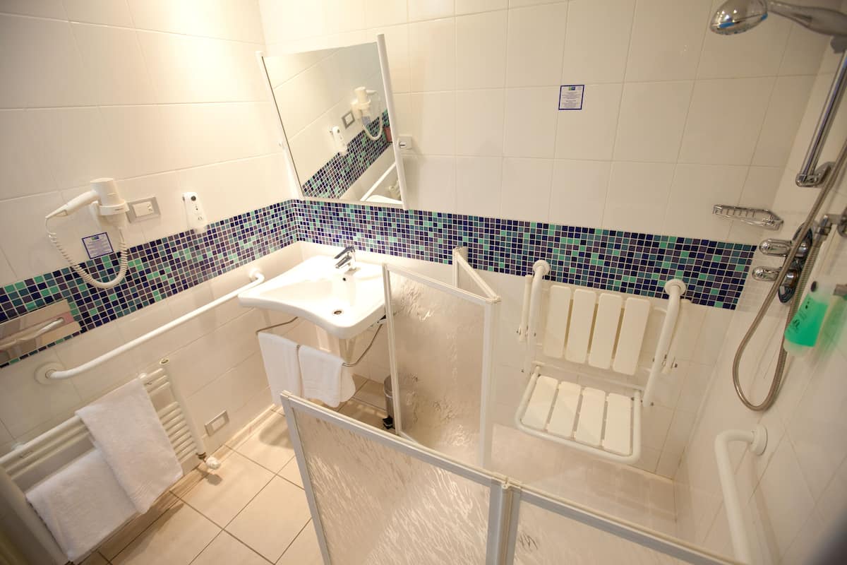 Une salle de bain avec un lavabo blanc, un miroir, une douche et un sol carrelé.