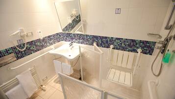 A bathroom with a white sink, a mirror, a shower, and a tiled floor.
