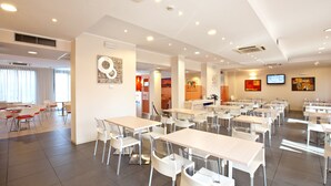 Un grand espace dédié à la salle à manger, avec plusieurs tables et chaises, un téléviseur fixé au mur et des œuvres d’art accrochées aux murs.