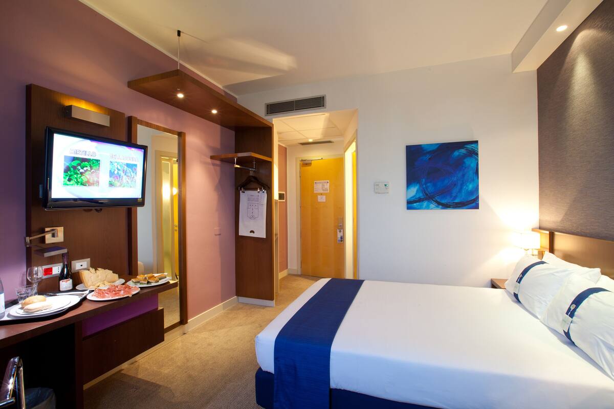 Une chambre d’hôtel comprenant un lit, une télévision, un bureau avec de la nourriture et des boissons, et une porte donnant sur une autre pièce.