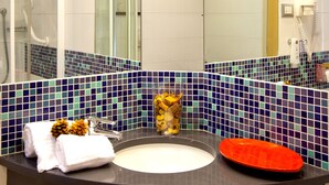 Un baño con un espejo grande, baldosas blancas, ducha y lavamanos con un respuesto de mosaico azul.