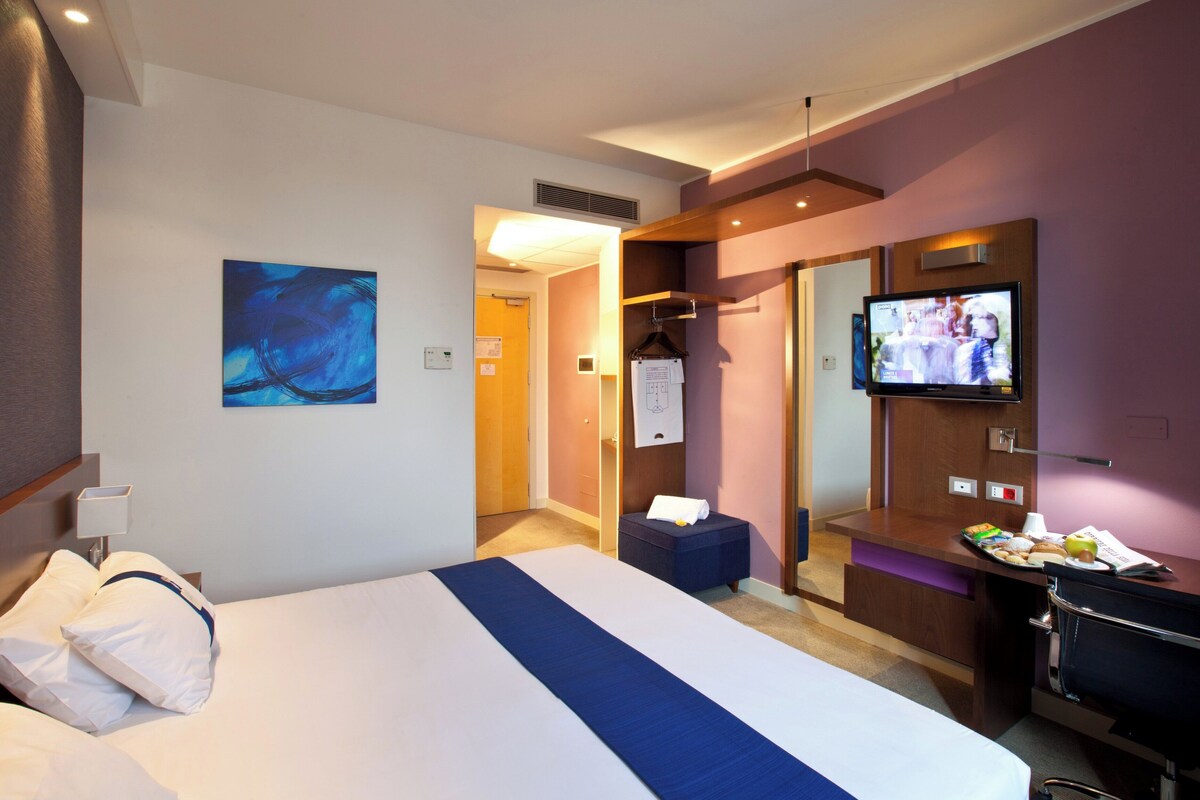 Habitación de hotel con cama, televisión, escritorio y puerta de baño.