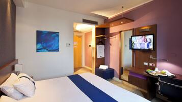 Habitación de hotel con cama, televisión, escritorio y puerta de baño.