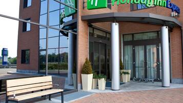 A Holiday Inn Express hotel entrance with a glass facade, a bench outside, and a clear sky.