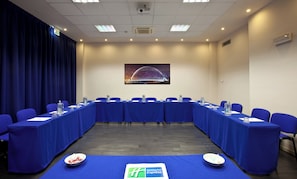 Une salle de conférence avec une longue table, des chaises bleues et le logo de l’hôtel Holiday Inn Express imprimé sur la nappe.