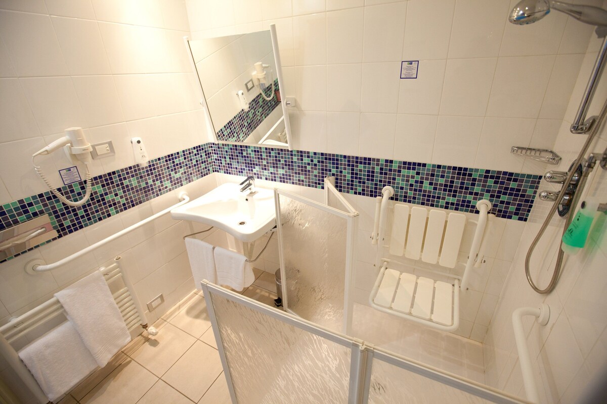 Un baño con lavamanos blanco, un espejo, ducha y suelo con baldosas.
