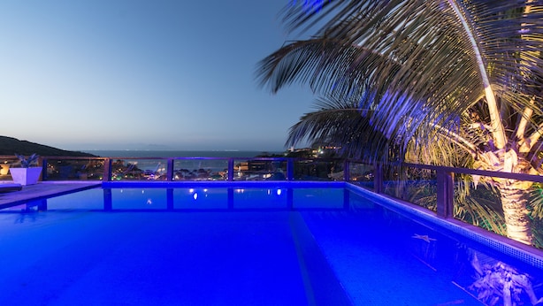 A swimming pool with a view of the ocean and city lights at dusk. - La Pedrera Small Hotel & Spa (Búzios)