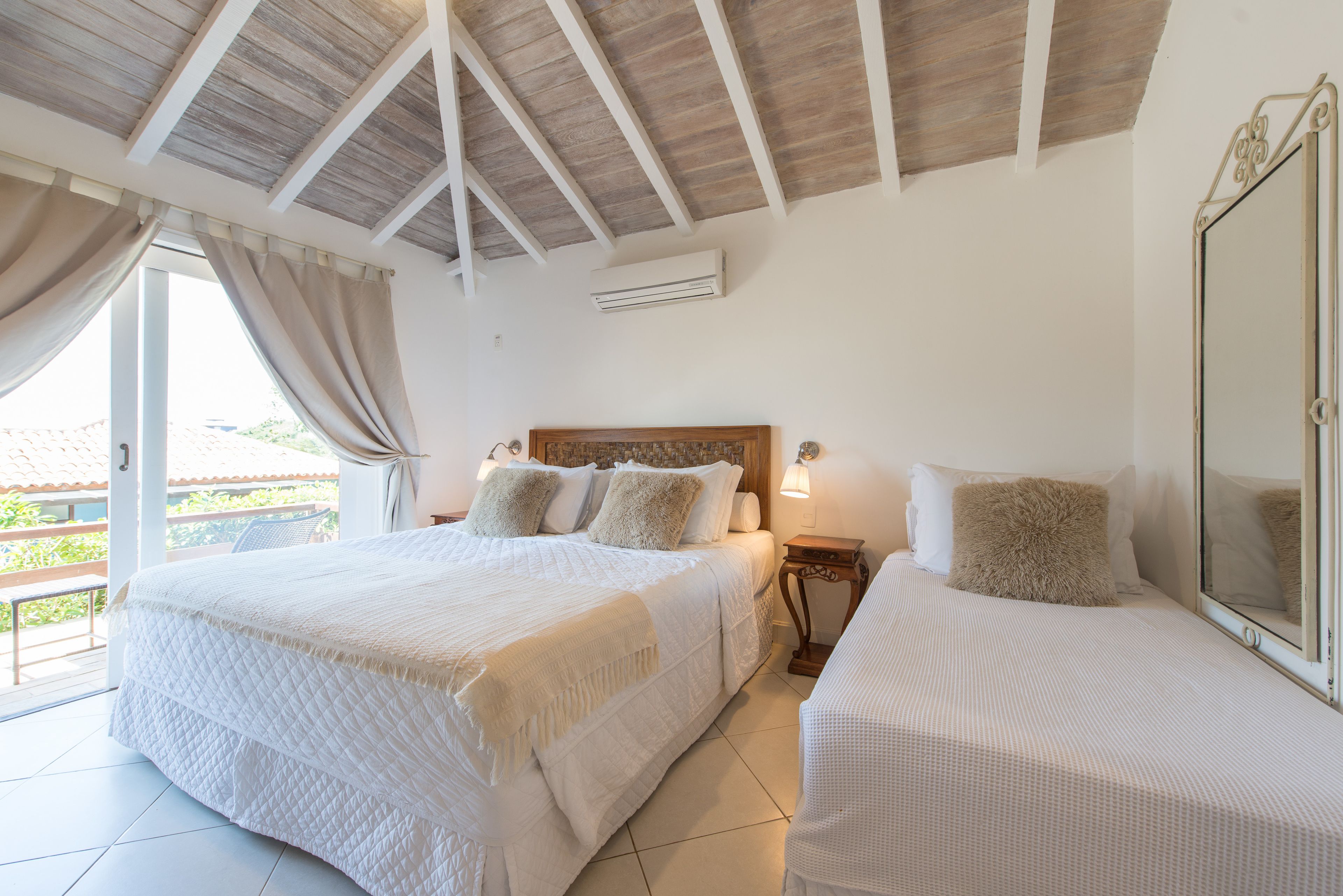 A bedroom with a large bed, a smaller bed, a nightstand, a mirror, and a window with curtains.