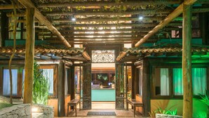 A wooden reception area with a tiled floor, a reception desk, and a decorative entrance with a green-lit backdrop. - La Pedrera Small Hotel & Spa (Búzios)