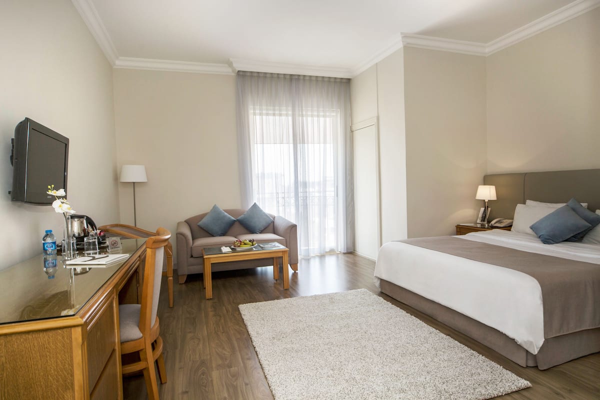 A hotel room with a bed, a desk with a TV, a sofa, and a coffee table.